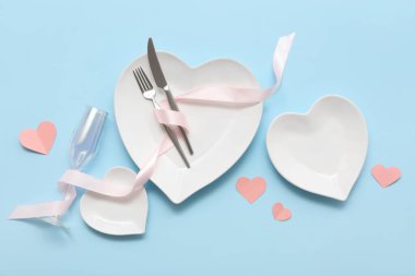 Kalp şeklinde tabaklar ve mavi arka planda kağıt kalplerle Sevgililer Günü için masa ayarı