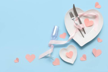 Kalp şeklinde tabaklar ve mavi arka planda kağıt kalplerle Sevgililer Günü için masa ayarı