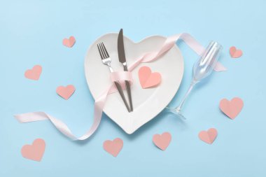 Kalp şeklinde tabaklar ve mavi arka planda kağıt kalplerle Sevgililer Günü için masa ayarı