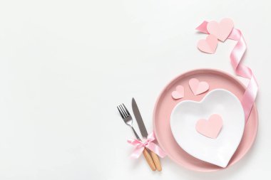Beyaz zemin üzerinde kağıt kalpler ve ipek kurdele ile Sevgililer Günü için masa ayarları