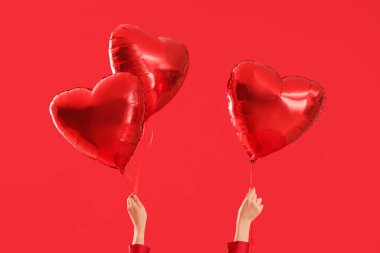 Kırmızı arka planda kalp şeklinde balonları olan kadın eller. Sevgililer Günü kutlaması