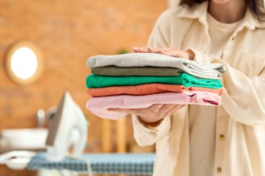 Güzel bir genç kadın, banyoda bir yığın elbisesi ve ütüsü var, yakın plan.