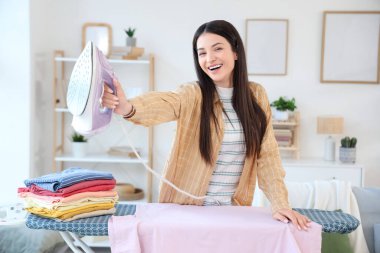 Evde demir ve giysi yığınıyla güzel, mutlu bir kadın var.