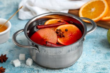 Elmalı, portakallı ve mavi arka planda farklı baharatlı sıcak sıcak şarap pişirmek.