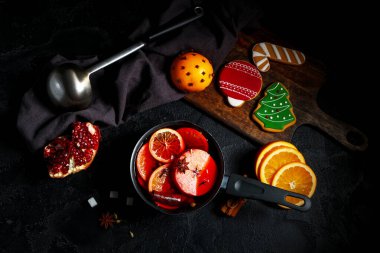 İçinde malzemeler ve siyah arka planda zencefilli kurabiye bulunan sıcak şarap tenceresi.