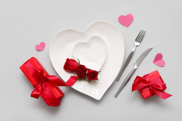 Накрытие стола на День Святого Валентина с тарелками в форме сердца, подарочными коробками и бумажными сердцами на белом фоне