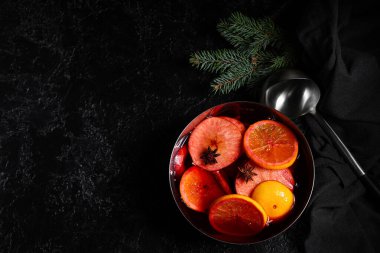 Siyah arka planda elma, portakal ve Noel ağacı dallarıyla sıcak sıcak şarap pişirmek.