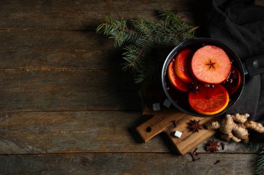 Farklı baharatlı sıcak şarap tenceresi ve ahşap arka planda Noel ağacı dalları.