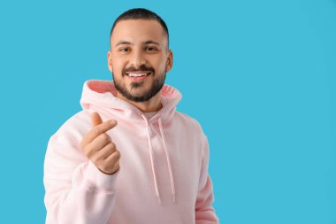 Yakışıklı genç adam mavi arka planda kalp hareketi gösteriyor.