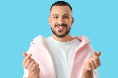 Yakışıklı genç adam mavi arka planda kalp hareketi gösteriyor.