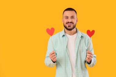 Sarı arka planda kağıt kalpli yakışıklı genç adam.