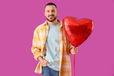 Mor arka planda kalp şeklinde balonu olan yakışıklı genç adam.