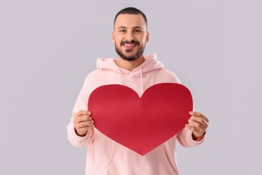 Gri arka planda kağıt kalpli yakışıklı genç adam.