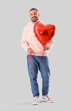 Gri arka planda kalp şeklinde balonu olan yakışıklı genç adam.