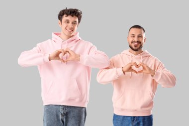 Gri arka planda kalp hareketleri gösteren yakışıklı genç adamlar.