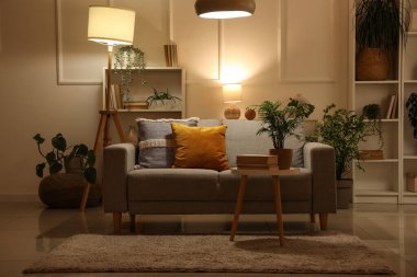 Yumuşak kanepe, sehpa ve gece oturma odasının içinde parlayan lamba.