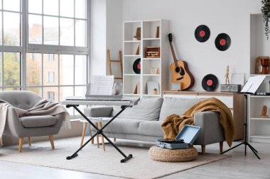 Aydınlık oturma odasının içinde sentezleyici, koltuk ve koltuk var.