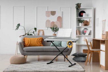 Aydınlık oturma odasının içinde sentezleyici, koltuk ve raf ünitesi var.