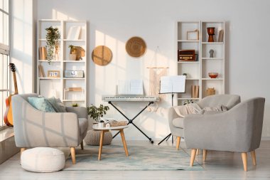 Aydınlık oturma odasının içinde sentezleyici, koltuk ve koltuklar var.