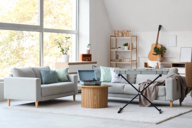 Oturma odasının içinde kanepeler, masa ve müzik aletleri var.