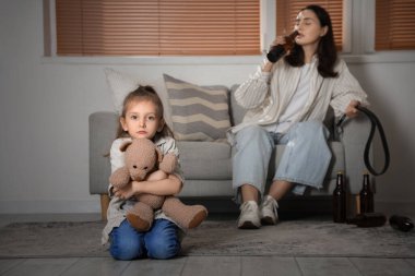 Oyuncak ayıyla üzgün küçük bir kız ve sarhoş annesi evde. Aile içi şiddet kavramı