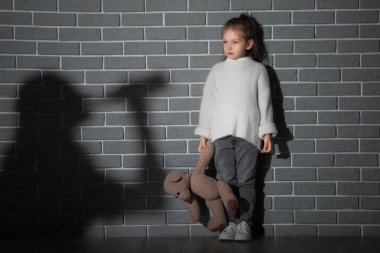 Gri tuğla duvarda oyuncak ve sarhoş annesinin gölgesi olan üzgün küçük bir kız. Aile içi şiddet kavramı