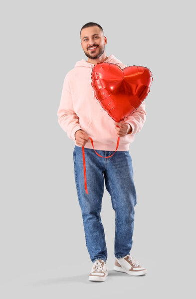 Красивый молодой счастливый человек с шаром в форме сердца на сером фоне