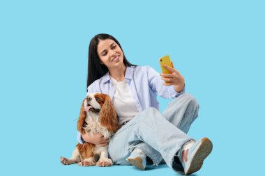 Güzel, genç bir kadın süvari Kral Charles Spaniel ile mavi arka planda selfie çekiyor.