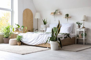 Rahat yataklı, komodinli ve çiçekli, aydınlık yatak odasının içi.