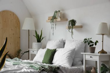 Rahat yataklı, komodinli ve çiçekli, aydınlık yatak odasının içi.