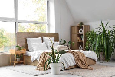 Rahat yataklı, komodinli ve çiçekli, aydınlık yatak odasının içi.