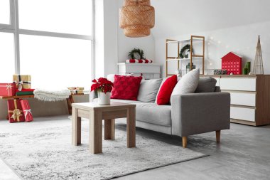 Masanın üzerinde kanepe ve Noel çiçeği süsleriyle aydınlık oturma odasının içinde.