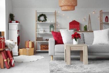 Masanın üzerinde kanepe ve Noel çiçeği süsleriyle aydınlık oturma odasının içinde.