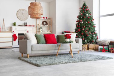 Masasında kanepe, köknar ağacı ve noel çiçeği olan aydınlık oturma odasının içi.