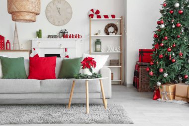 Masasında kanepe, köknar ağacı ve noel çiçeği olan aydınlık oturma odasının içi.