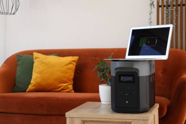 Oturma odasında dizüstü bilgisayarı ve bitkisi olan taşınabilir elektrik santrali.
