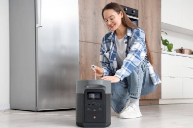 Buzdolabını mutfaktaki taşınabilir elektrik santraline bağlayan genç bir kadın.
