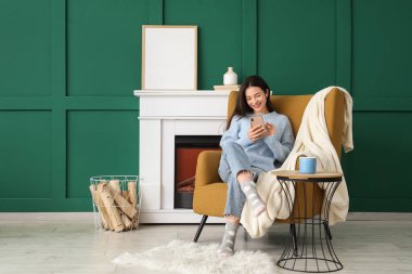 Kışın evde koltukta cep telefonu kullanan genç bir kadın.