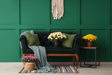 İçinde yeşil kanepe ve kasımpatı çiçekleri olan oturma odası.