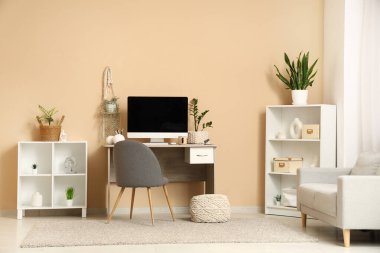 Bej duvarın yanında bilgisayar ve bitkilerin bulunduğu modern işyeri