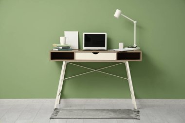 Laptop, lamba ve yeşil duvarın yanında kitapları olan modern işyeri