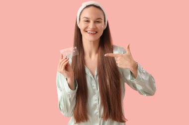 Pembe arka plandaki sivilce yamalarını gösteren pijamalı genç bir kadın.