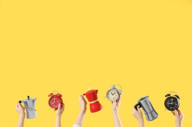 Çalar saatli kadın eller ve sarı arka planda kahve makineleri. Günaydın konsept.