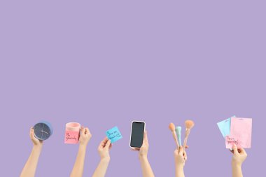 Çalar saati olan kadın eller, motivasyonlar, cep telefonu ve eflatun arkaplanda makyaj malzemeleri. Günaydın konsept.