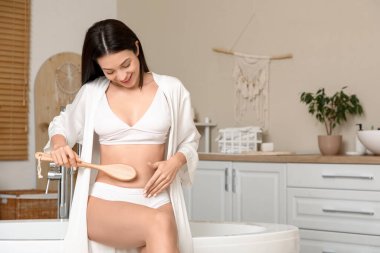 Masaj fırçalı güzel, genç, mutlu bir kadın banyoda oturuyor.