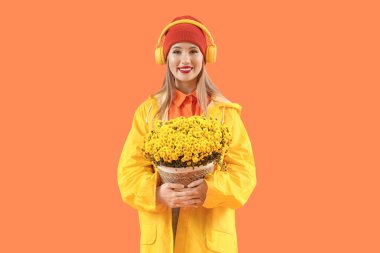 Kulaklık takan ve turuncu arka planda kasımpatı çiçekleri olan genç bir kadın.