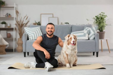 Avustralyalı çoban köpeği olan genç bir adam evde minderde oturuyor.