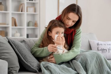 Hasta küçük kız hapşırıyor ve annesi evdeki kanepede termometreyle yatıyor.