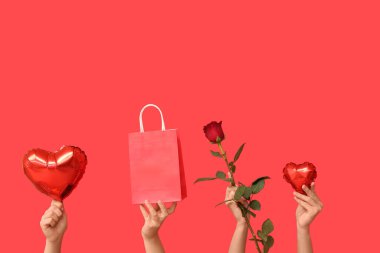 Kalp şeklinde balonları, kese kağıdı ve kırmızı arka planda kırmızı gül olan kadın elleri. Sevgililer Günü kutlaması