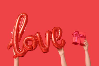 Balon şekilli kadın elleri. Aşk kelimesi ve kırmızı arka planda hediye kutusu. Sevgililer Günü kutlaması